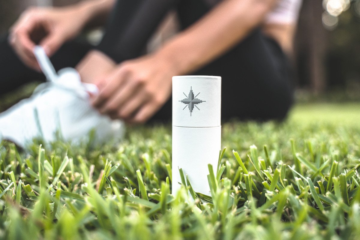 Canvas 1839 Relief Oil impressed us by offering pure, unadulterated CBD oil relief. Photo: A cardboard tube containing Canvas 1839 Relief Oil rests in the grass outside, with a person sitting in the background behind them.